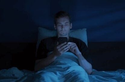 Mann scrollt nachts im Bett im bläulichen Licht seines Smartphones