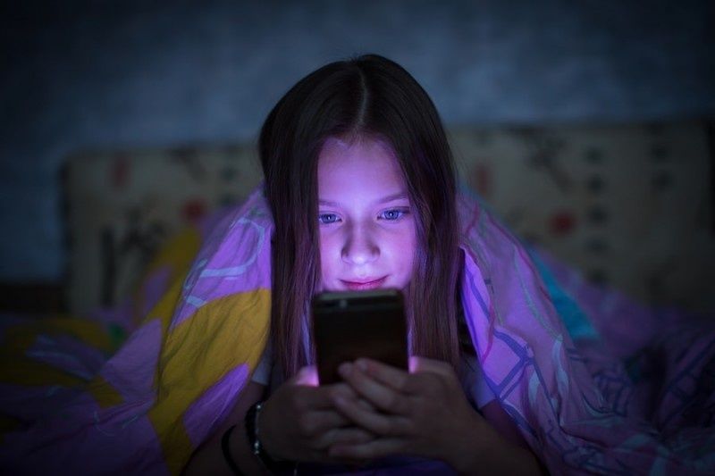 Mädchen liest nachts im Bett gebannt auf einem leuchtenden Smartphone